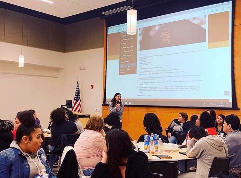 woman speaking and presenting to a group of people in front of a projector screen