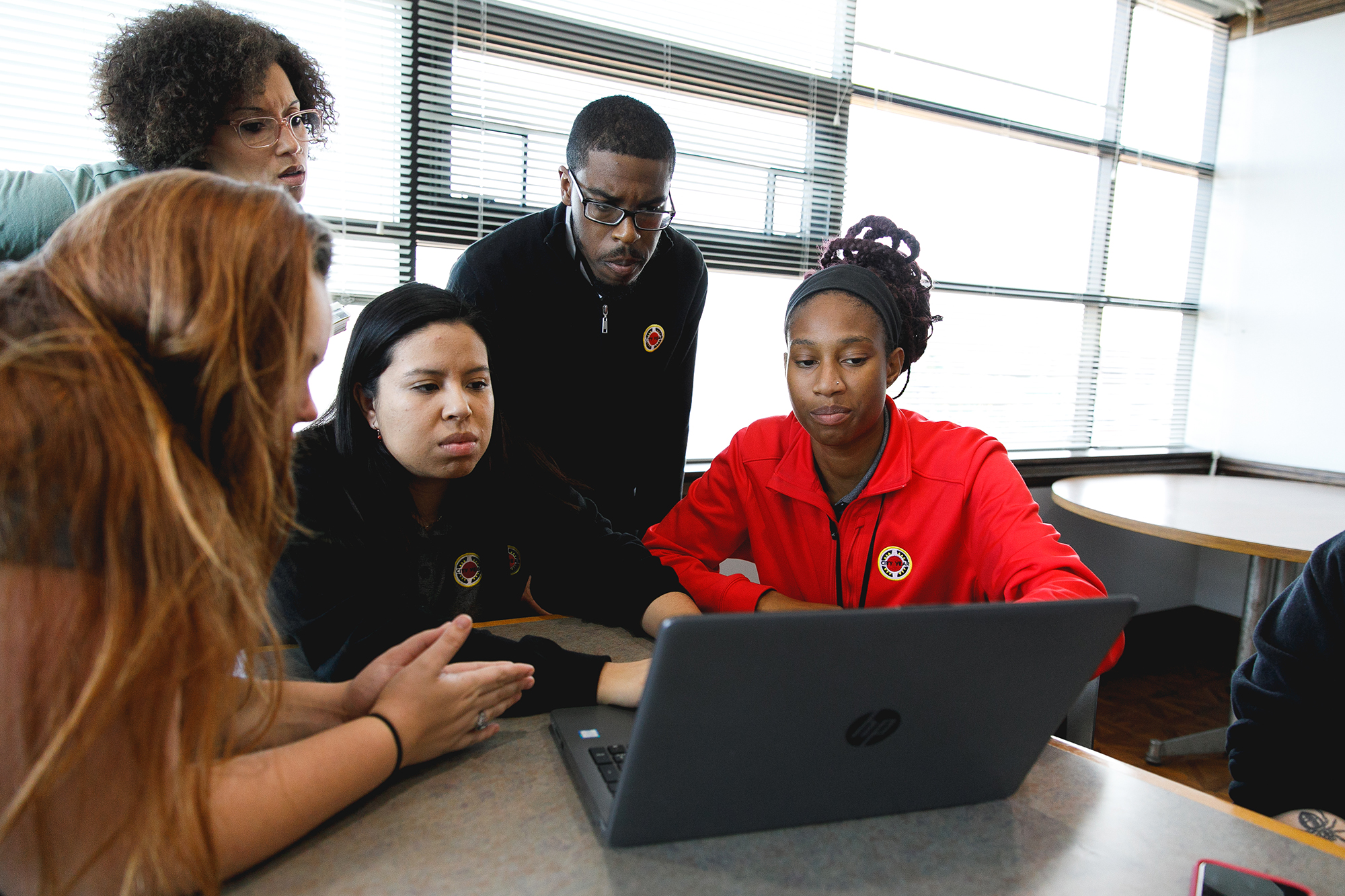 group of people standing around a table looking at a laptop