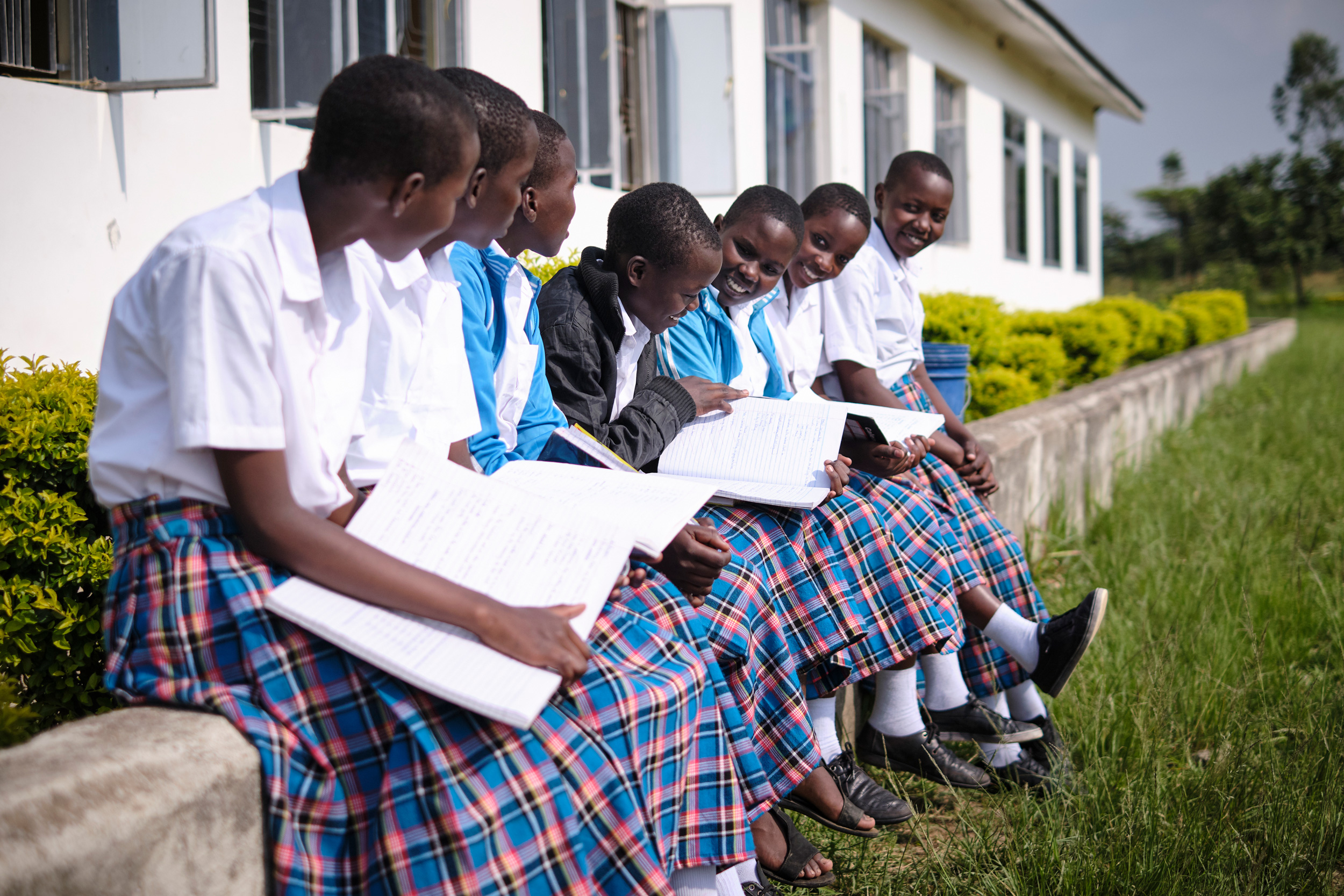 group of girls sitting on a retaining wall looking at each other and their notebooks