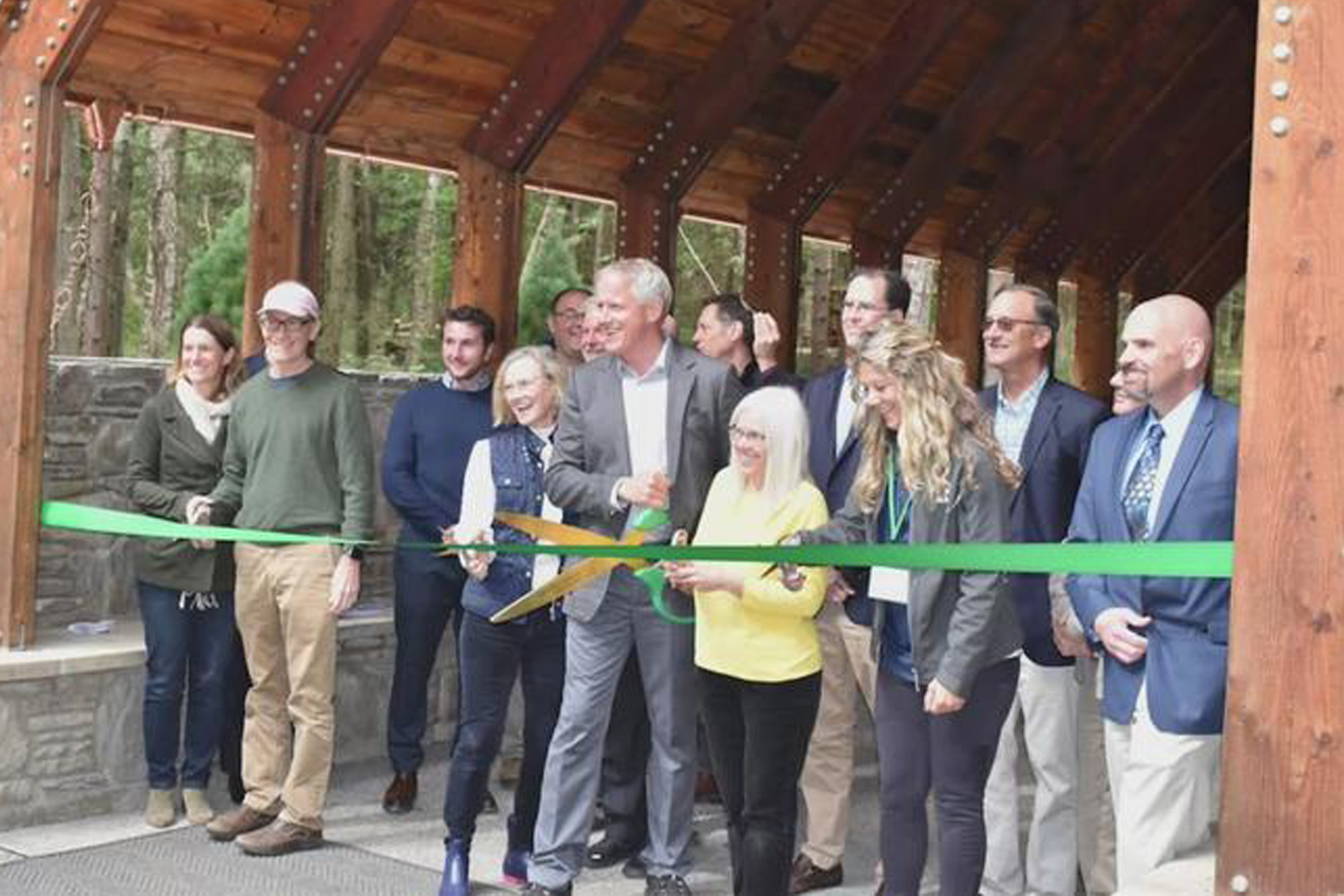 group of people standing together getting ready to cut a green ribbon