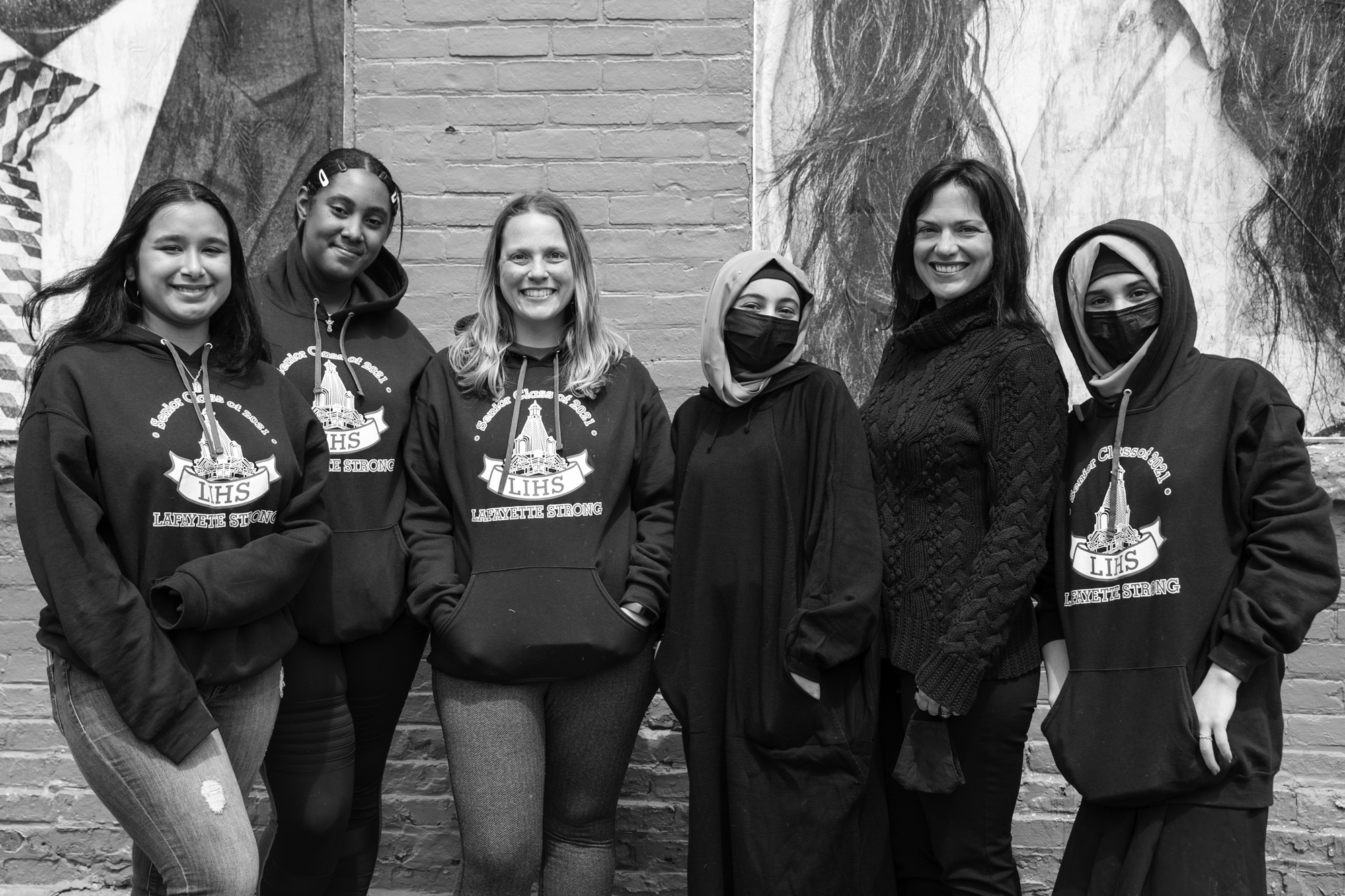 black and white photo of a group of women smiling in front of the portraits on the brick building