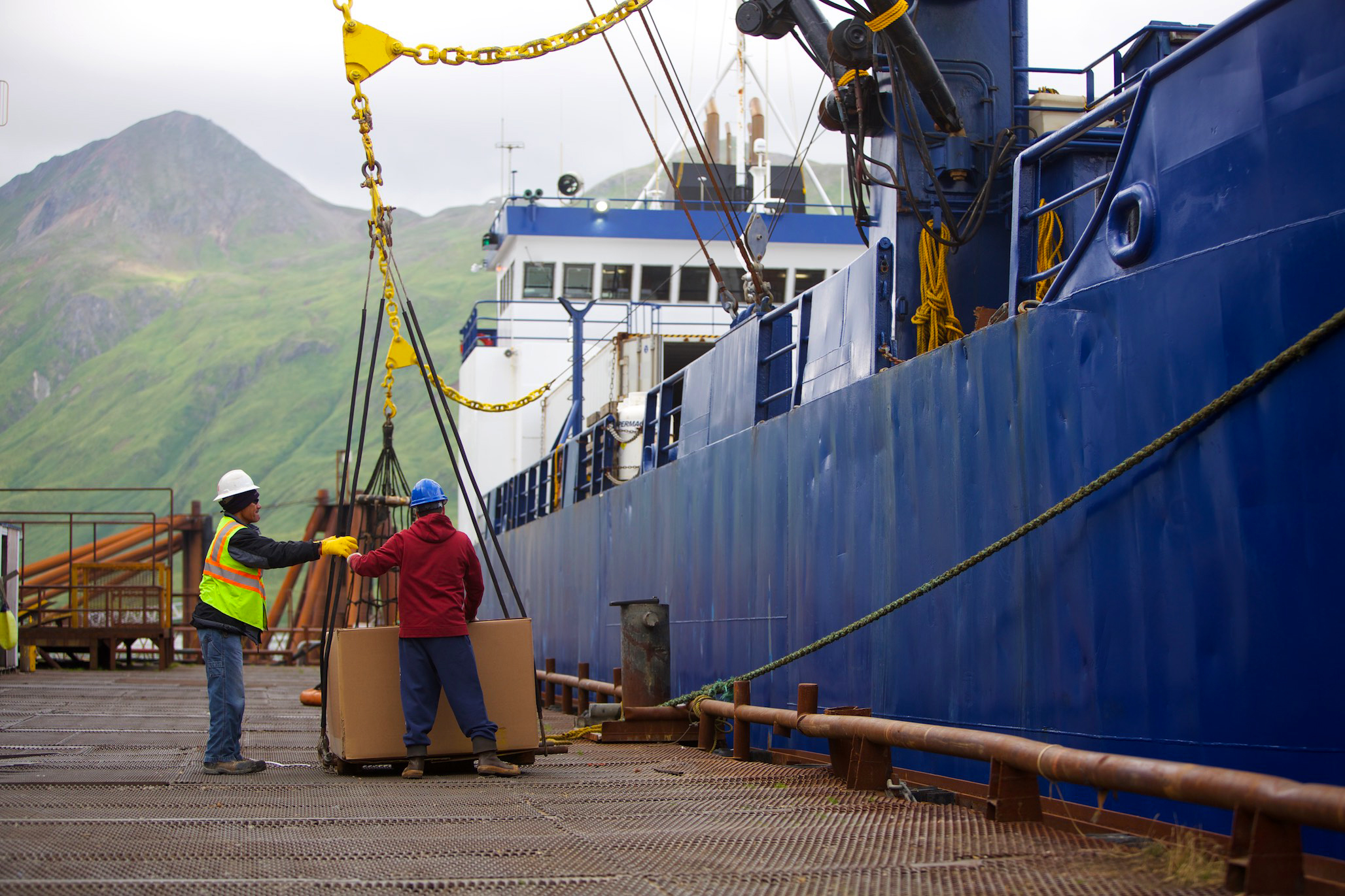 two men using a crane to load cardboard boxes onto a boat