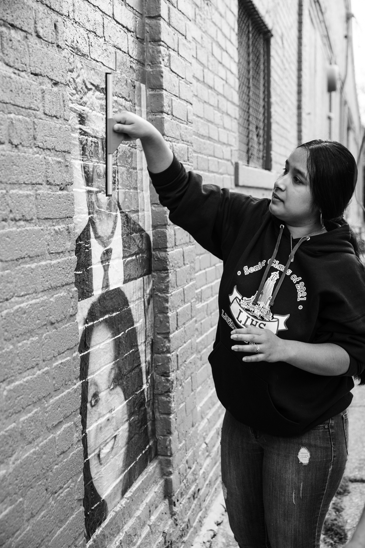 woman pressing person's portrait print onto the side of a brick building